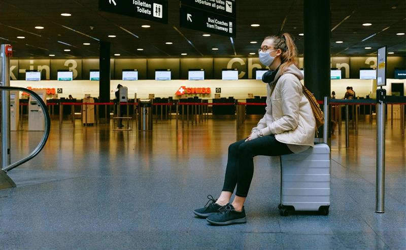 a woman with a face mask waits in airport - crisi management for destinations